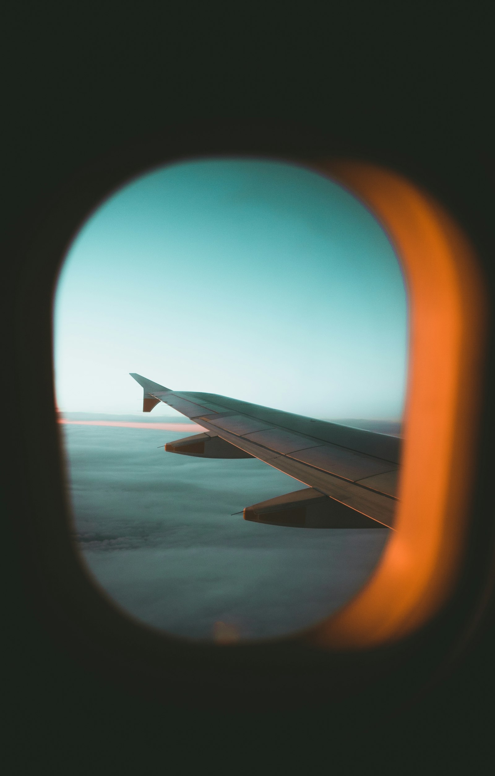 A wing and horizon seen through a cabin window at dusk